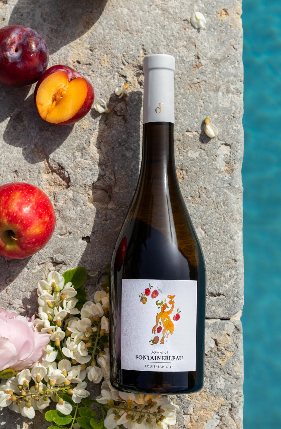 Une bouteille de la collection Héritage au bord de la piscine, entre fruits et fleurs — Domaine Fontainebleau en Provence