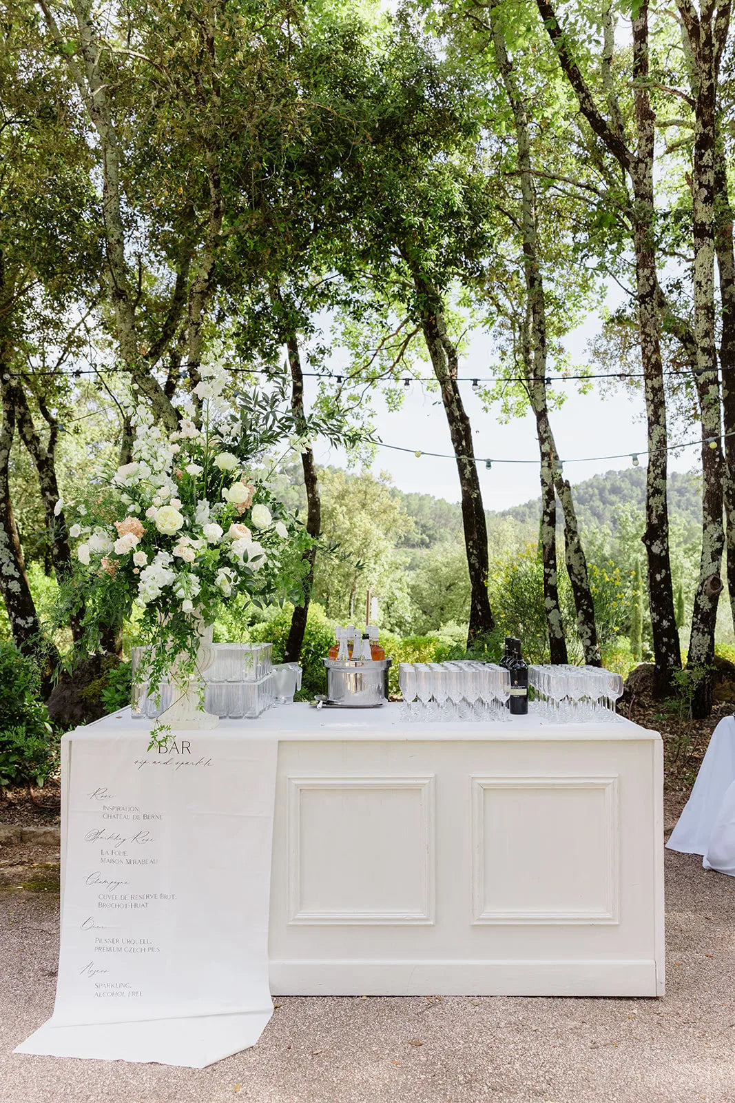 Un bar de réception blanc fleuri, sous les arbres — Domaine Fontainebleau en Provence