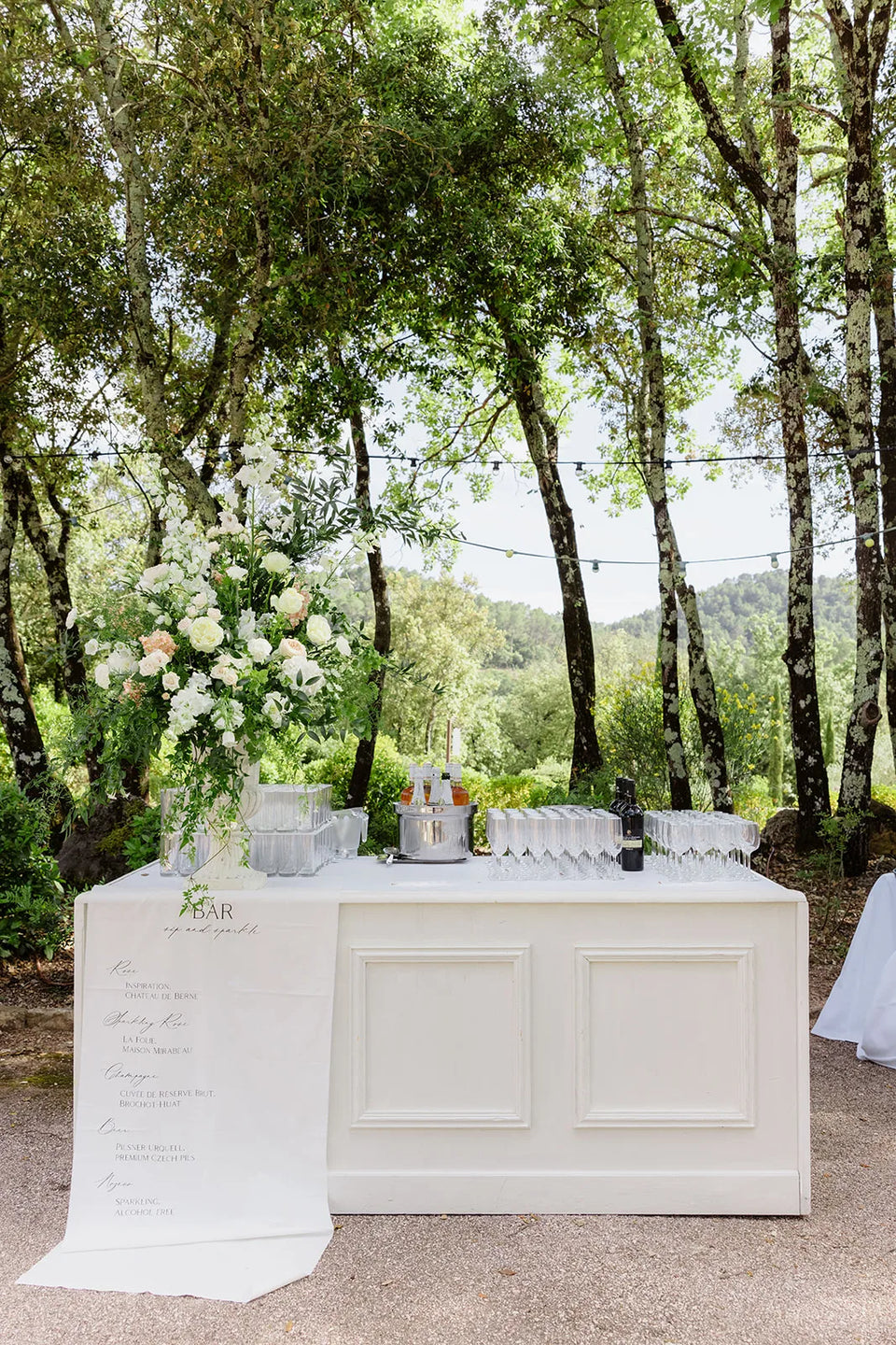 Un bar de réception blanc fleuri, sous les arbres — Domaine Fontainebleau en Provence